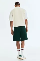 Short de corte relajado de color verde oscuro, con cintura elástica y cordón ajustable. Cuenta con ribetes de cinta blanca a lo largo de los laterales y bolsillos frontales.
