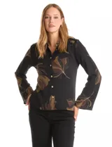 Camisa de crepe con estampado floral en tonos verdes y marrones sobre fondo negro. Presenta cuello con solapa, cierre frontal con botones dorados y hombros con detalle de mostacillas bordadas. Las mangas son largas con terminación amplia.