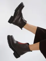 Botinetas de cuero negro con diseño combinado en gamuza y cuero texturizado. Presentan cierre frontal central, suela track dentada con costuras visibles en contraste y caña media.