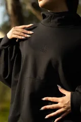 Canguro negro oversize de algodón, con capucha amplia, cuello alto integrado y ruedo ajustable con tancas.