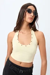 Top halter color marrón, con escote redondeado y detalle de ojales metálicos a lo largo del cuello. Presenta un diseño ajustado al cuerpo y espalda descubierta.