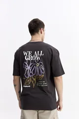 Remera de manga corta color crema con cuello redondo y fit regular. Presenta un estampado grande en la espalda con una flor estilizada en tonos rojo y azul, y texto que incluye "WE ALL GROW" y "trust the process, great things take time".