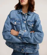 Campera de jean con corte boxy, cuello clásico, cierre frontal con botones metálicos, bolsillos con solapa en el pecho y costuras reforzadas.