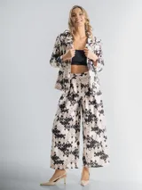Conjunto de dos piezas compuesto por un blazer de corte recto con solapas y un pantalón de tiro alto y pierna ancha. Ambas prendas están confeccionadas en tela con estampado floral en tonos neutros. El blazer incluye un aplique floral desmontable.
