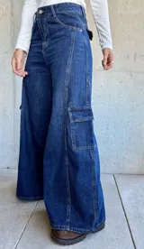 Pantalón tipo jean cargo de corte ancho y tiro alto, confeccionado en denim azul oscuro. Presenta bolsillos laterales tipo cargo con solapa y costuras reforzadas a lo largo de las piernas.