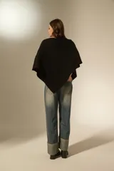 Poncho negro de tejido de punto con diseño asimétrico y detalle de pequeñas aplicaciones brillantes distribuidas por toda la superficie. Presenta un borde acanalado en el ruedo.