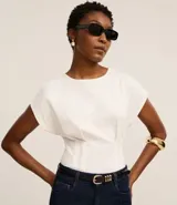 Blusa blanca de algodón con cuello redondo y mangas cortas. Presenta pliegues delanteros y traseros con efecto corsetado.