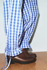 Pantalón de nylon con estampado de cuadros vichy azul y blanco. Presenta cintura elástica y bajo con volante fruncido y elástico.