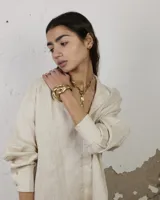 Brazalete abierto de diseño orgánico y voluminoso, con acabado metálico brillante. Su forma irregular y ergonómica permite un ajuste cómodo en la muñeca o antebrazo.