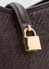 Bolso tipo bucket de tamaño pequeño, confeccionado con tejido de rafia color marrón con efecto texturizado y detalles en cuero sintético liso del mismo tono. Cuenta con un asa corta superior, herrajes metálicos dorados, cierre de imán y un detalle decorativo con candado dorado en la parte frontal.