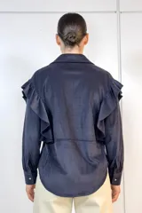 Camisa de pana fina color negro, con volados decorativos en los hombros y a lo largo de la botonadura frontal. Presenta cuello clásico, mangas largas con puños abotonados y botones dorados frontales.