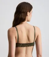 Soutien tipo bralette confeccionado en encaje con textura floral, diseño de escote en V, breteles finos ajustables y detalle de medalla metálica en el centro.