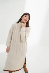 Vestido midi de tejido de punto color crema, con cuello alto, mangas largas y corte recto con aberturas laterales.