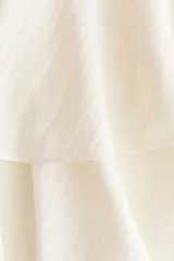 Pollera corta blanca con diseño asimétrico de dos capas de volados, donde la capa inferior se extiende formando un panel drapeado largo hacia un costado.