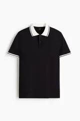 Polo de manga corta confeccionado en piqué de algodón, con cuello y bordes de mangas en color blanco con detalles de líneas negras. Presenta cierre frontal con botones y un corte ajustado.