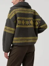 Sweater polar de cuello alto y cierre medio con detalles en cuero sintético, de color verde oscuro con estampado de patrones tradicionales en tono verde claro. Cuenta con mangas largas y diseño holgado.