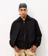 Campera boxy de poliéster color beige, con cuello inglés, cierre frontal de cremallera, mangas largas con elástico en los puños, bolsillos laterales y detalles de recortes.