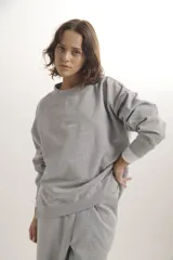 Sweater de cuello redondo, confeccionado en algodón gris melange, con diseño holgado y bordado sutil en el centro del pecho.