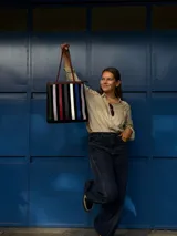 Cartera tipo tote de cuero con diseño de franjas verticales multicolores en tonos tierra, rojo y azul. Cuenta con correas trenzadas de cuero y cierre superior.