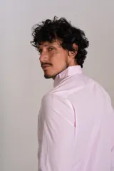 Camisa de manga larga confeccionada en tejido poplin con diseño de rayas verticales finas en color rosado y blanco. Presenta cuello abotonado (button-down), cierre frontal con botones y un bolsillo en el pecho.