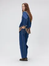 Campera de jean estilo cazadora con corte crop, cierre frontal con botones metálicos, bolsillos delanteros con apliques, bordados y detalles de tachas metálicas en el pecho.