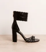 Sandalias de tacón alto en color negro, confeccionadas en 100% cuero vacuno. Presentan un diseño elegante con tiras finas en la parte delantera y una pulsera ancha en el tobillo con cierre de cremallera en la parte trasera. Cuenta con un taco ancho.