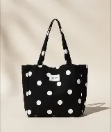 Tote bag de algodón color negro con estampado de lunares blancos. Cuenta con doble asa de hombro y etiqueta frontal con el logo de la marca.