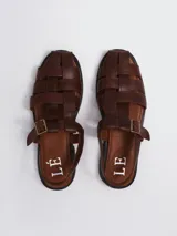 Sandalias tipo pescador de cuero marrón, con diseño de tiras entrelazadas, cierre con hebilla lateral y suela plana.