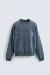 Sudadera de corte boxy fit con efecto lavado, cuello redondo y manga larga. Presenta estampados a contraste en color violeta en la parte frontal y acabados en rib en cuello, puños y ruedo.