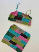 Conjunto de dos piezas tejido a crochet con diseño de bloques de colores. Incluye un top tipo crop con breteles finos y una pollera corta con cordón ajustable en la cintura con detalles de cuentas de madera.