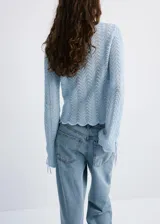 Buzo de punto celeste con diseño recto, detalles calados, cuello redondo y manga larga con cordones ajustables en los puños.