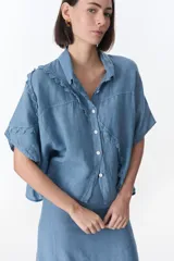 Camisa color beige de lino con cuello camisero, manga corta y cierre frontal con botones. Presenta detalles de encaje en el cuello, el frente y las mangas.