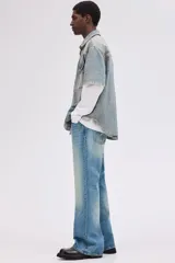 Jean de cinco bolsillos en denim de algodón rígido, tiro alto, con cierre y botón. Corte estándar con pierna acampanada amplia. Presenta un lavado celeste claro con efecto degradado o tie-dye en la parte inferior de las piernas.