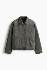 Campera de denim de algodón rígido, color gris oscuro con efecto gastado, cuello clásico, hombros caídos y cierre frontal. Cuenta con bolsillos delanteros ribeteados, un bolsillo superior con cierre y bajo recto.