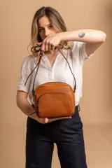 Bandolera de diseño compacto en color beige, confeccionada en material símil cuero con textura granulada. Cuenta con un bolsillo frontal con cierre y correa larga regulable.