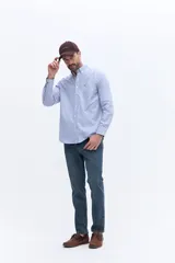 Camisa de corte regular confeccionada en tejido oxford de algodón, con diseño de rayas verticales en azul y blanco. Presenta cuello abotonado, cierre frontal con botones, mangas largas con puños abotonados y un pequeño logo bordado en el pecho.
