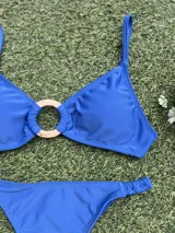 Bikini de dos piezas color azul vibrante. El corpiño es tipo top con un detalle de hebilla redonda dorada en el centro. La bombacha es colaless entera con frunces ajustables en los laterales.