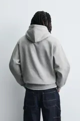 Sudadera tipo hoodie de corte relajado, confeccionada en tejido de algodón con interior cepillado. Presenta capucha con cordones ajustables, bolsillo frontal tipo canguro y terminaciones en rib en puños y ruedo.