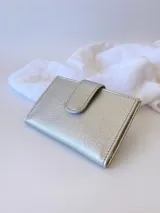 Tarjetero plateado de cuero con broche a presión. Tiene espacio para 4 tarjetas y billetes, y un bolsillo externo.