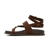 Sandalias planas Korium Adhara de cuero color marrón oscuro con tiras de gamuza en tono tostado. Presentan diseño de tira al dedo, tachas doradas y abalorios de piedras incrustadas, y tira ajustable al tobillo con hebilla metálica.