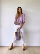 Bolso tipo tote de cuero color lila con textura croco, detalles en cuero marrón y laterales con franjas blancas. Incluye manijas de cuero marrón y accesorio de borlas colgantes.