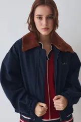 Campera bomber de paño color azul marino, con cuello de piel sintética en color marrón desmontable, cierre frontal y puños elásticos. Presenta logo bordado en el frente y bolsillos laterales.