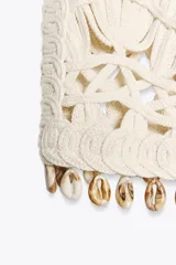 Chaleco abierto de punto color crudo con manga sisa y detalle de conchas en el ruedo.