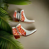 Botas de caña corta de cuero blanco con detalles pintados a mano en tonos coral, rojo y naranja. Cuentan con taco cuadrado de madera, doble cierre lateral con tiradores personalizados y punta fina.