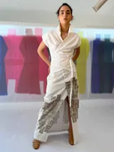 Falda larga blanca de lino y algodón con estampa exclusiva en cobre laminado. Corte asimétrico, tajo central y un bolsillo lateral. Cierre frontal con broches a presión.