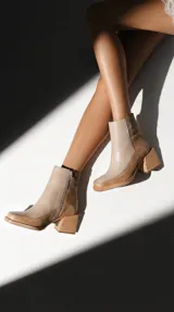 Botineta de cuero con diseño bicolor en tonos beige y marrón, con cierre lateral y taco cuadrado de madera de diseño geométrico.