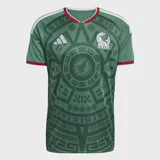 Camiseta de fútbol Adidas de la selección de México, primera equipación 2026. Diseño en color verde con estampado gráfico inspirado en la cultura azteca, detalles en blanco y rojo en el cuello y las mangas, logo de la marca y escudo de la selección en el pecho.