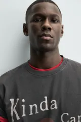 Camiseta de manga corta y cuello redondo, color negro con efecto lavado. Presenta un estampado frontal con un corazón rojo y texto en blanco que dice "Kinda Care Kinda Don't".