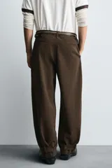 Pantalón de algodón color marrón oscuro, estilo balloon fit, con talle alto, cierre frontal y trabillas ajustables en los bajos. Presenta costuras verticales marcadas en el frente de cada pierna.