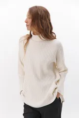 Polera de tejido acanalado en color blanco, con cuello alto, mangas largas y diseño de corte recto con aberturas laterales en el ruedo.